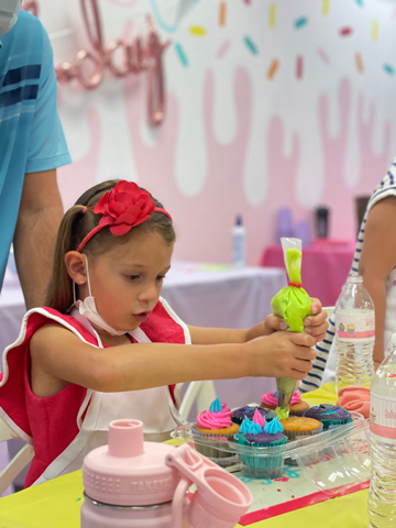 Child putting frosting on cupcakes at a birthday party