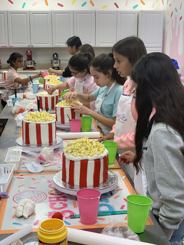 Children make a popcorn themed cake in baking class